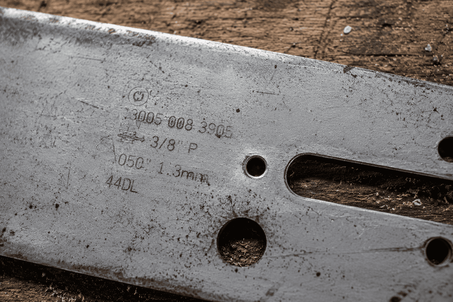 Close-up of a chainsaw guide bar showing stamped specifications including bar length, pitch and gauge markings